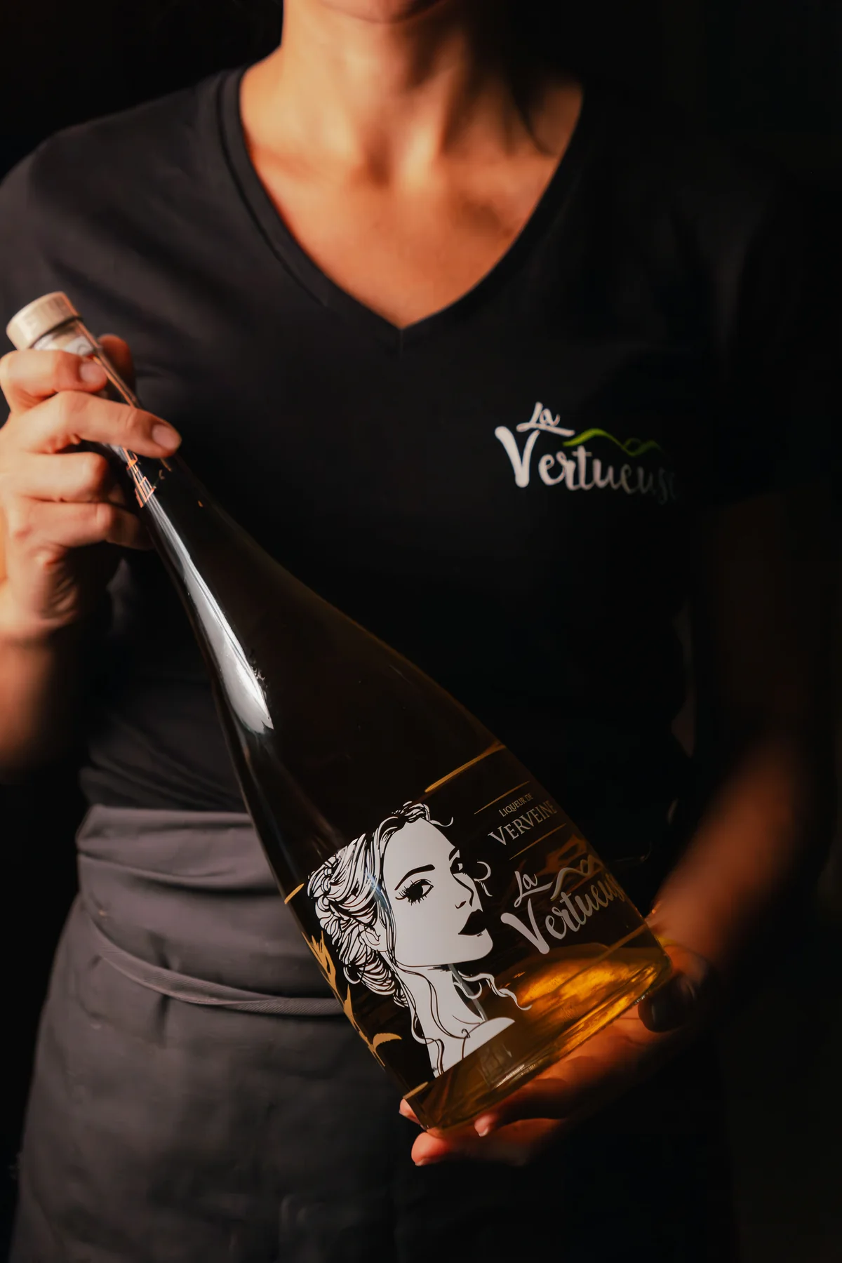 Une personne de l’équipe présente une bouteille de liqueur La Vertueuse